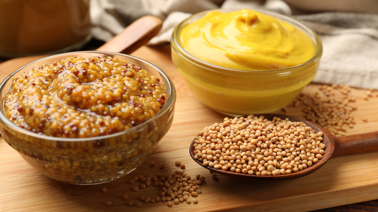 different types of mustard in small glass bowls on a wooden cutting board