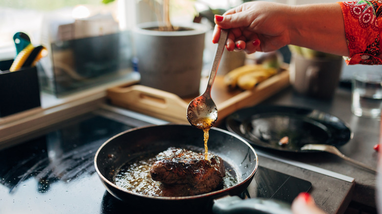a woman's hands pouring sauce over meat in a pan