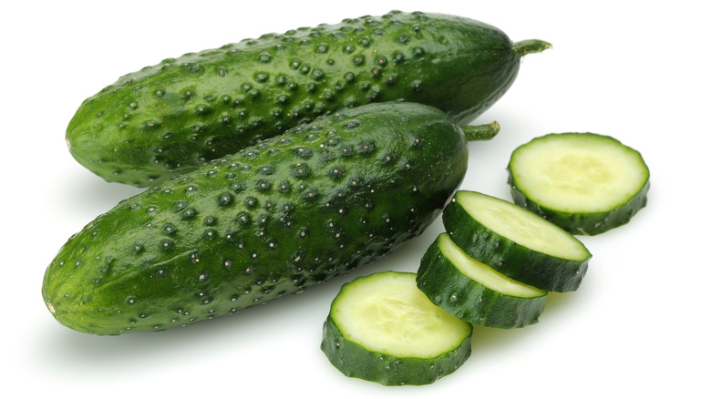 Two whole mini cucumbers beside a sliced cucumber
