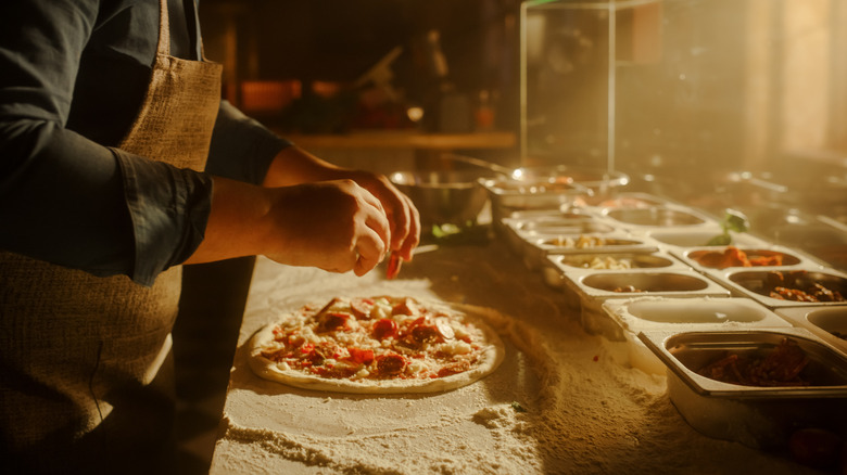 an apron-clad chef adding toppings to a small pizza