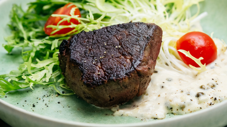 well-done steak on plate  with lettuce and tomatoes