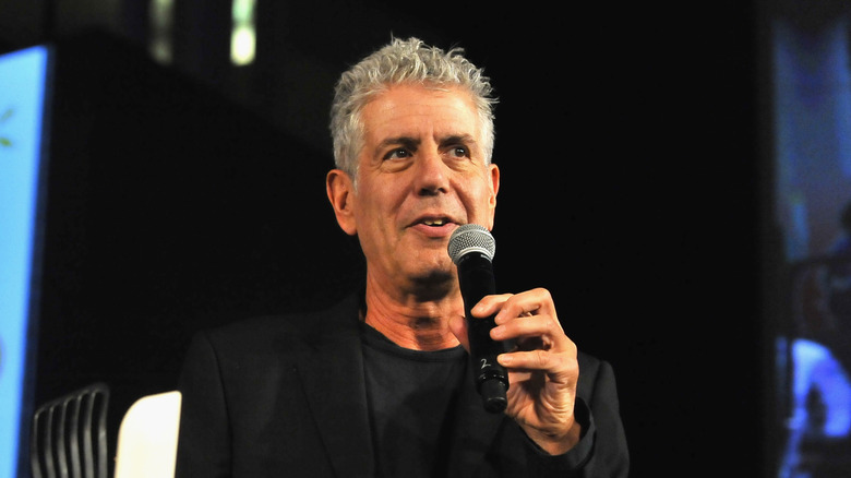 Anthony Bourdain, dressed all in black, speaking into a microphone