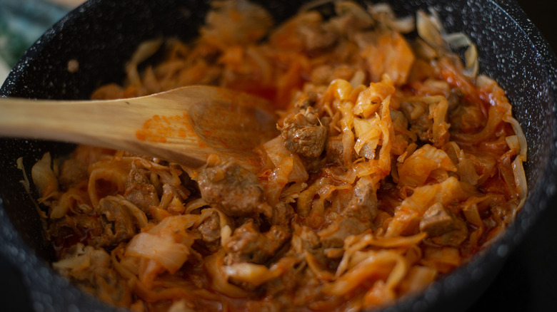 Closeup of braised cabbage stewing in a pan with onions and meat