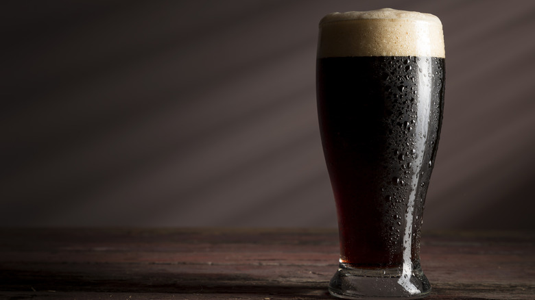 Glass of cold, dark stout with foam against brown background