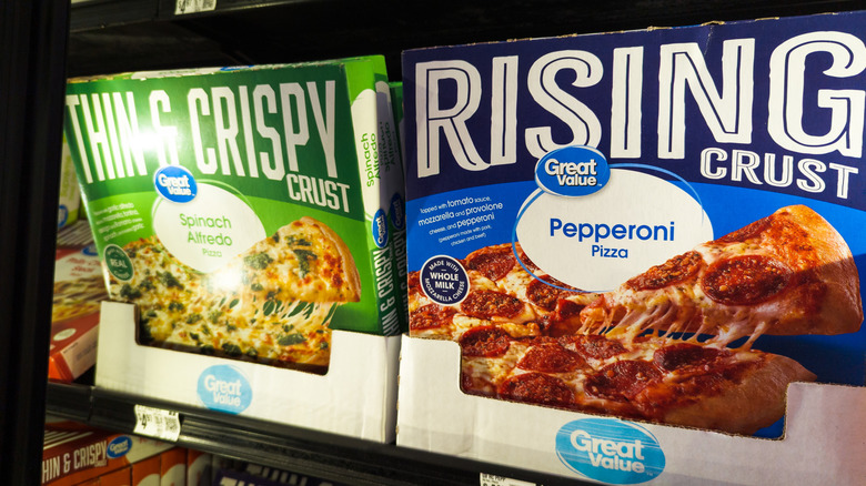 A box of Great Value Thin & Crispy Spinach Alfredo Frozen Pizza on a shelf next to a Great Value Rising Crust Pepperoni Frozen Pizza