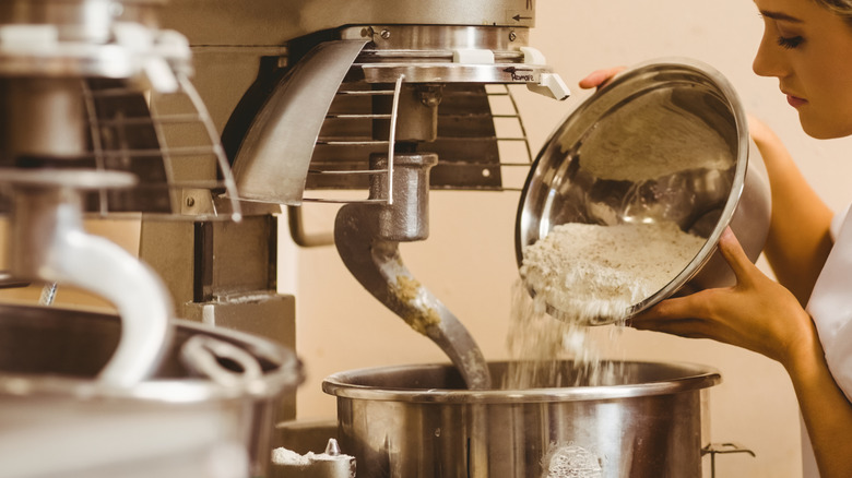 A baker pouring flour into an industrial mixer