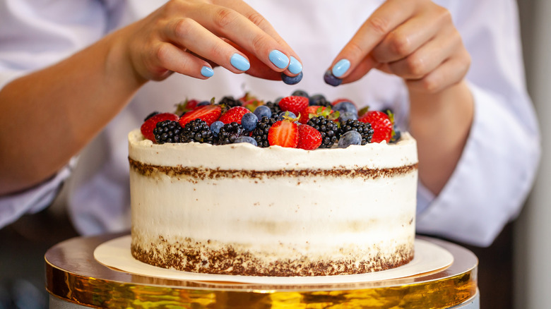 A chef decorating a frosted cake with fresh fruit