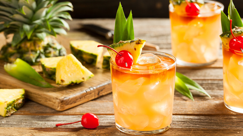 Three Mai Tai cocktails on a table, garnished with cherries and pineapple
