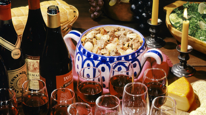1970s tureen of beef stroganoff surrounded by bottles of wine, retro home dinner party concept