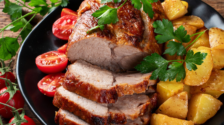 well done pork with tomatoes and roast potatoes on a black plate