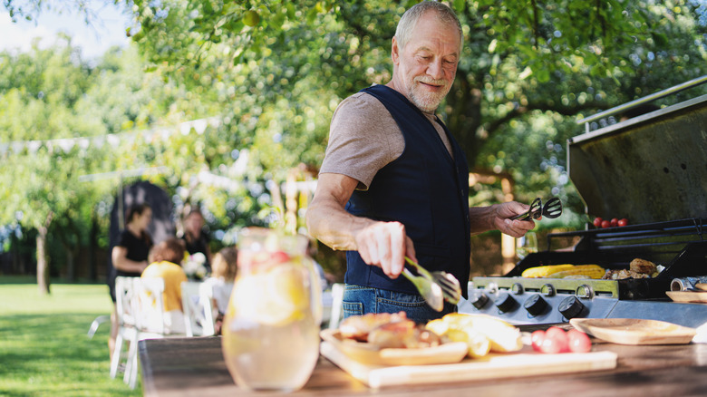 A man holding grilling tongs as he barbecues at on a summer evening