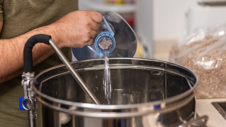 Hands filling a large stainless steel pot for beer making