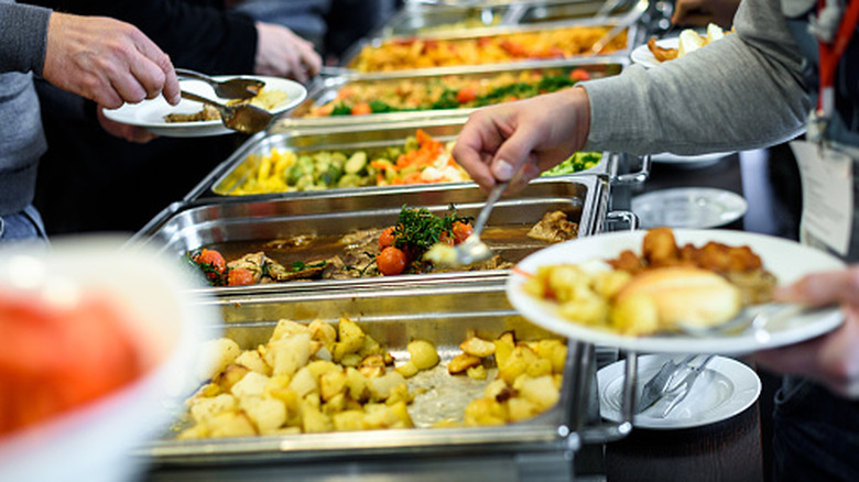A buffet with several people reaching in to dish up food