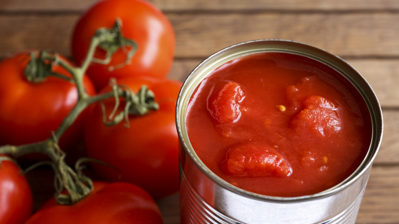 Open can of tomatoes next to whole fresh tomatoes