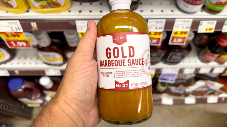 a hand holding up a bottle of gold sauce in a store