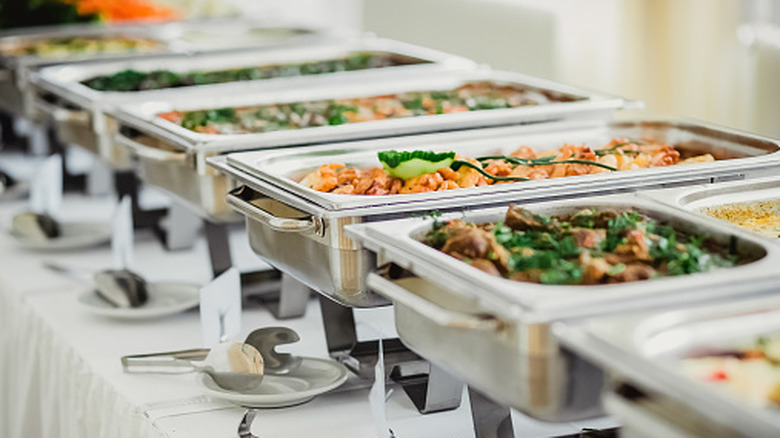 A line of metal chafing dishes filled with food at a buffet
