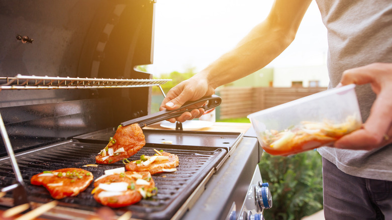 guy adds marinated meat to gas grill with tongs