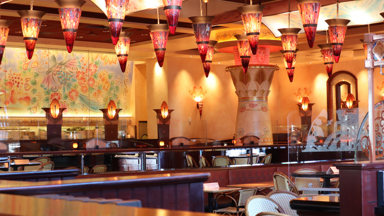 The interior of a Cheesecake Factory restaurant with dramatic hanging glass lamps and a large artwork on a wall