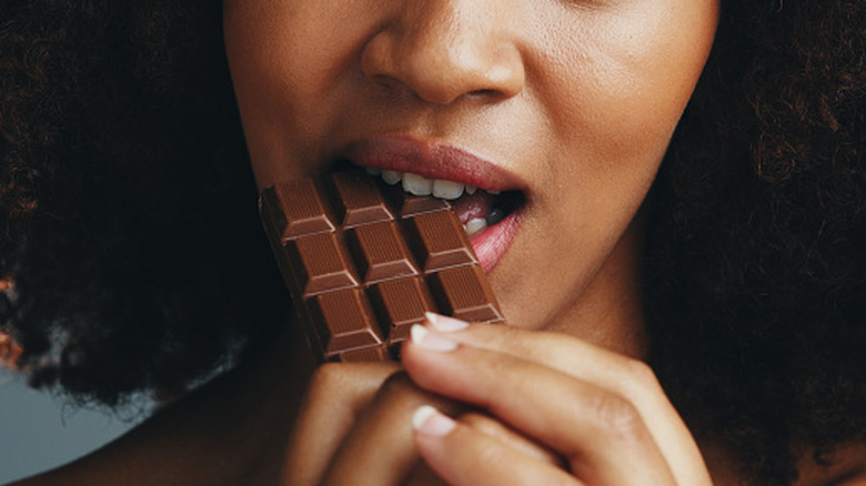 a close-up of a woman taking a bite from a bar of chocolate