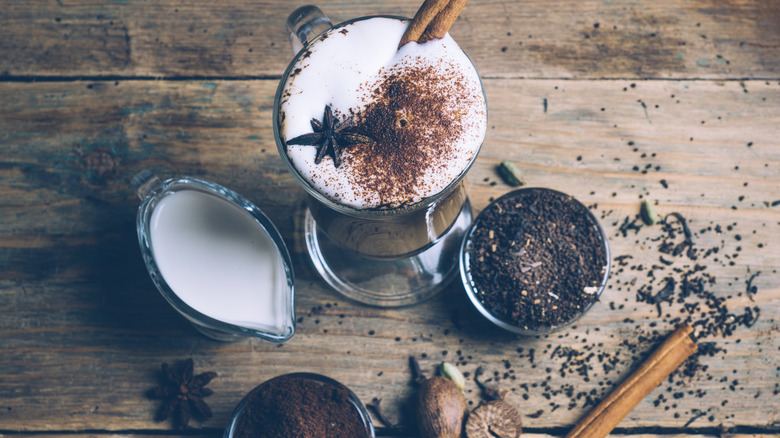 overhead view of dirty chai latte on wooden board with spices and coffee and tea on table