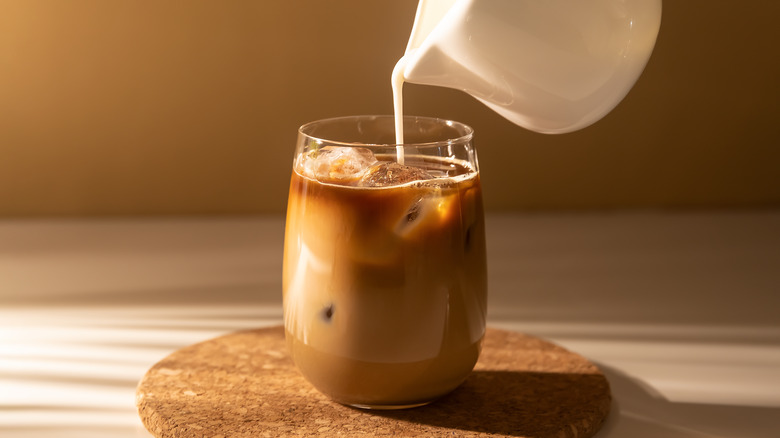 Milk being poured into a glass of coffee 