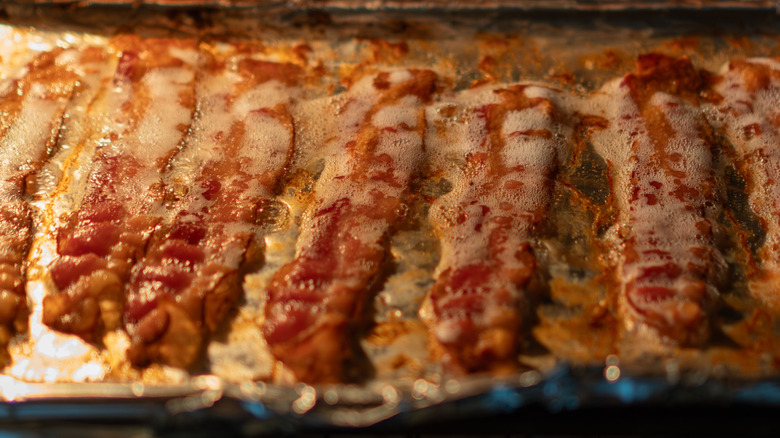 bacon cooking on a foil-lined sheet pan