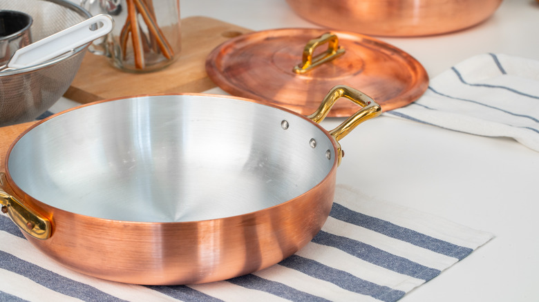 lined copper pan on a striped tea towel with another copper lid and other kitchen tools in the background.