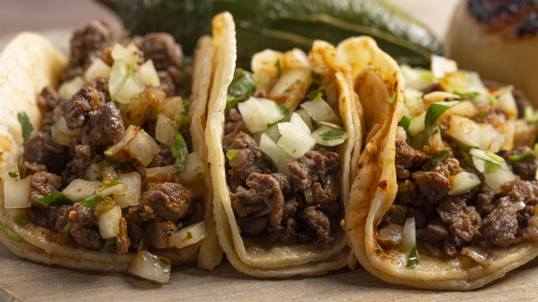 A trio of tacos filled with steak, onion, and cilantro served on double tortillas