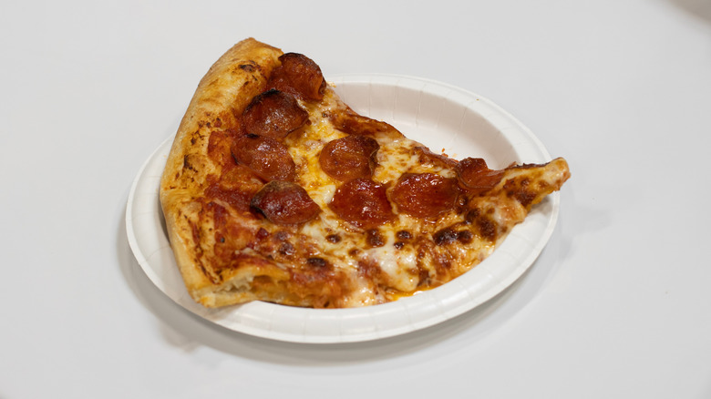 Slice of Costco food court pepperoni pizza on paper plate sitting on white surface