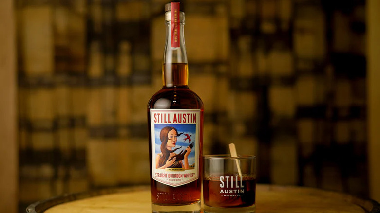 A bottle of Still Austin Bourbon Whiskey next to a poured glass.