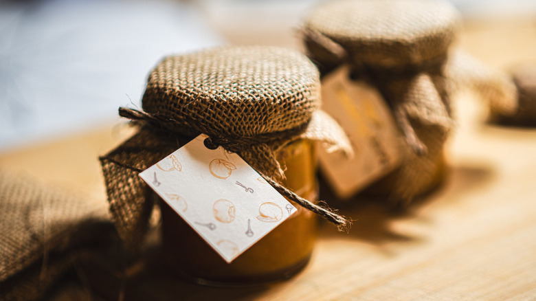 Jars of jam are topped with burlap fabric.