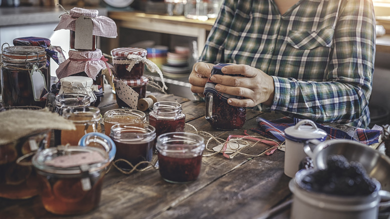 A woman ties fabric onto freshly made jars of jam.