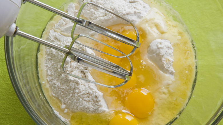 Overhead view of hand mixer atop cake mix with eggs and oil in a bowl