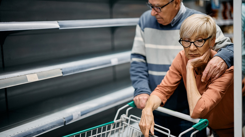 Older couple looking dismayed at empty shelves in grocery store