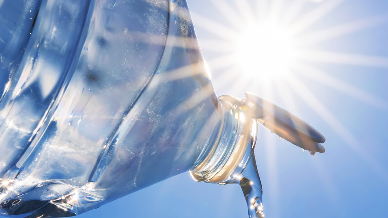 A bottle of water being poured out with the sun in the background