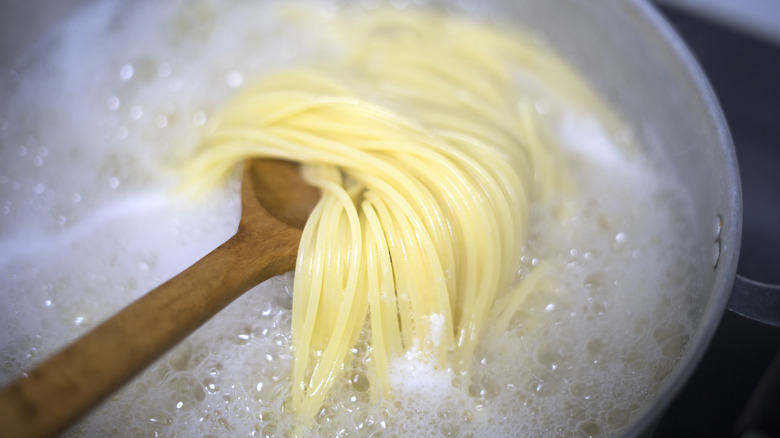 Wooden spoon holding spaghetti above pasta water