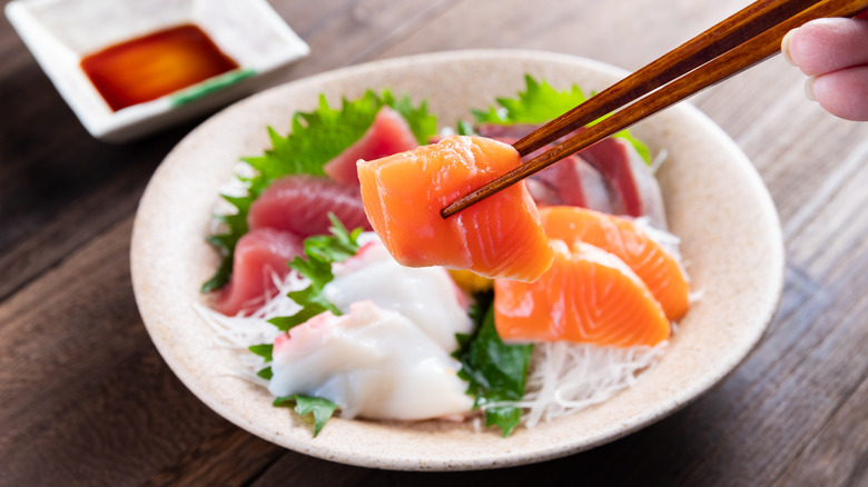 chopsticks pick up piece of raw salmon from sashimi bowl