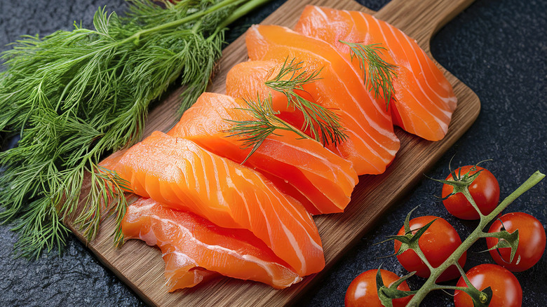 Cut raw salmon filets on a board with dill and tomatoes
