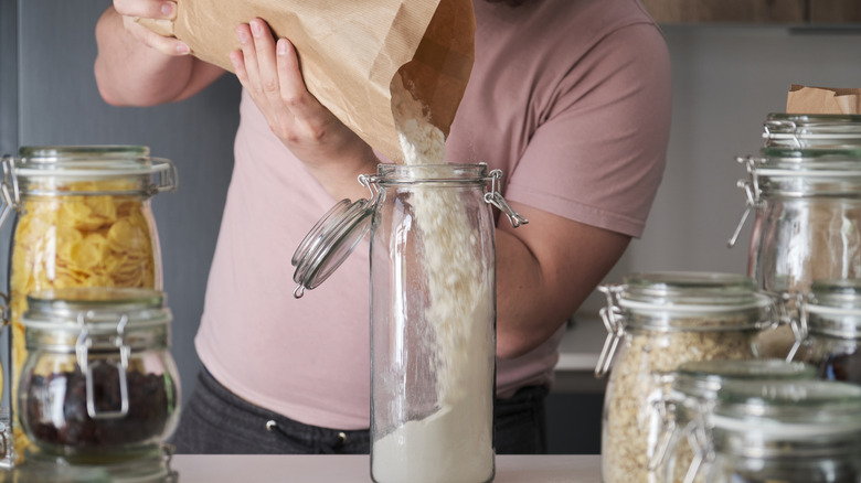 Man pouring flour from bag into a glass jar