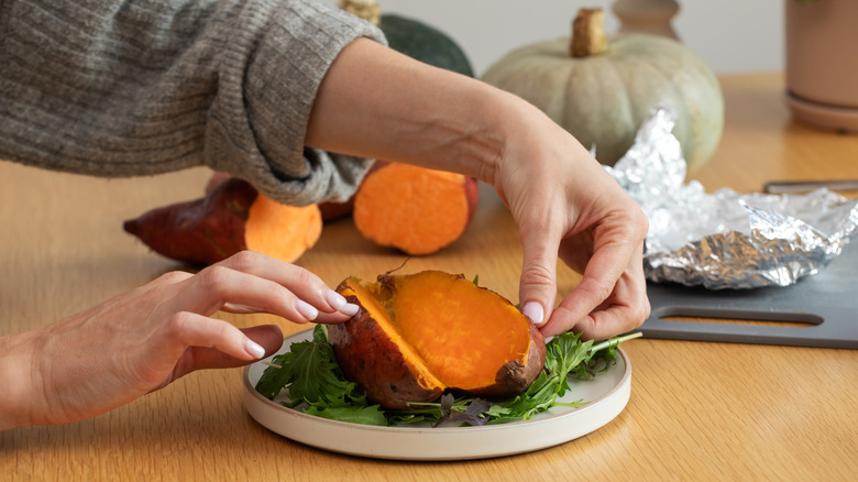 close up of a woman cutting into a baked sweet potato wrapped in foil