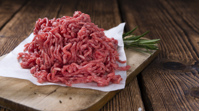 Freshly ground mince on a wooden board, with a sprig of rosemary on the side