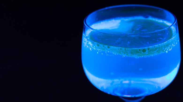 a glass of tonic water with a lemon slice glowing under black light