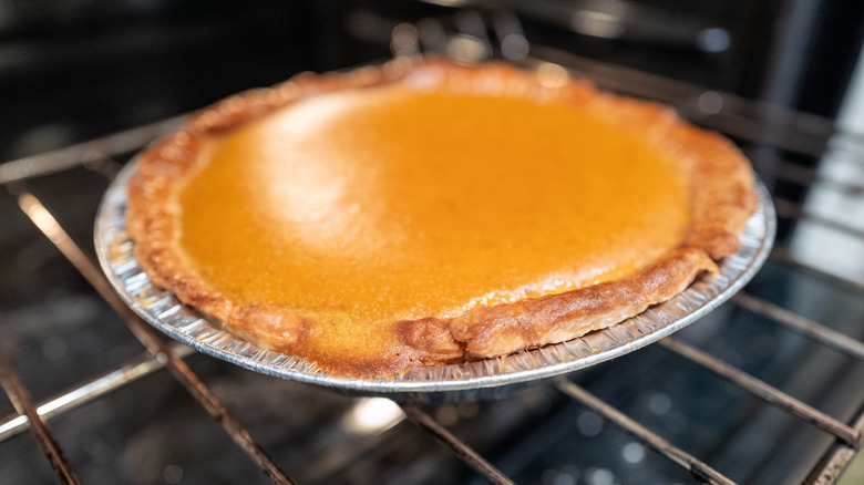 A pumpkin pie sits on a wire rack in an oven