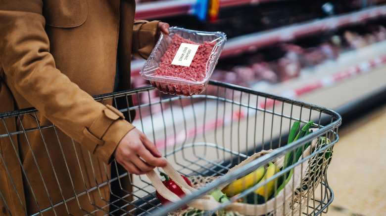 Person placing package of ground beef in shopping cart
