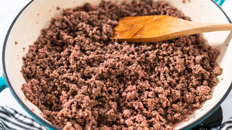 Ground beef cooking in skillet with wooden spoon