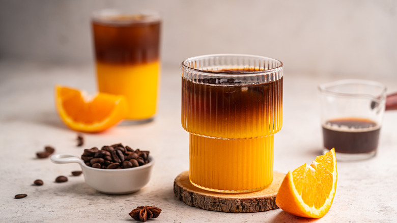 Coffee with orange juice aside sliced oranges and whole coffee beans.