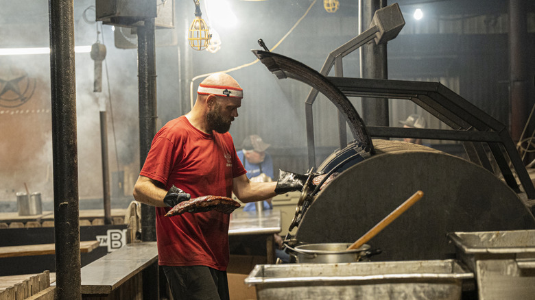 A pitmaster prepares to put a rack of ribs into a large smoker