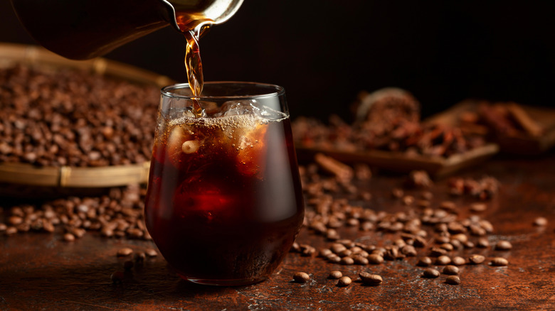 Pouring French press coffee into a glass over ice