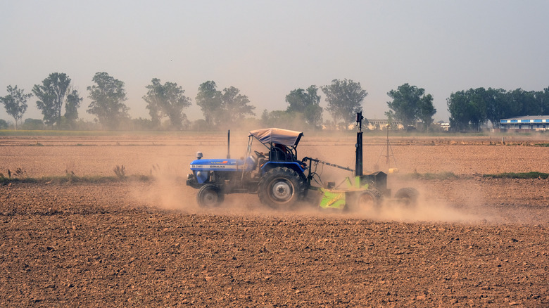 a wheat farmer in India works a field with a tractor