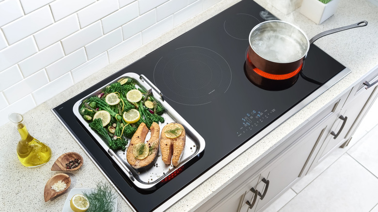 Tray of salmon steaks and vegetables heating on induction alongside a pot of boiling water